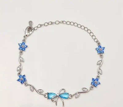 A silver chain bracelet featuring blue rhinestone flower motifs and a bow-shaped blue centerpiece, displayed on a plain light background.