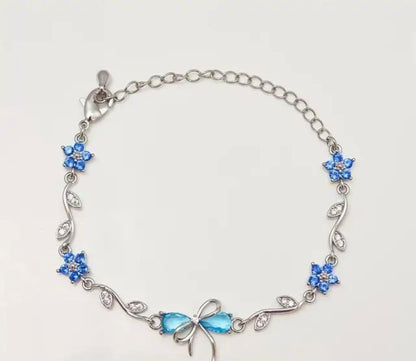 A silver chain bracelet featuring blue rhinestone flower motifs and a bow-shaped blue centerpiece, displayed on a plain light background.