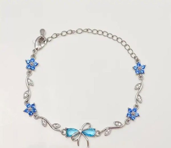 A silver chain bracelet featuring blue rhinestone flower motifs and a bow-shaped blue centerpiece, displayed on a plain light background.