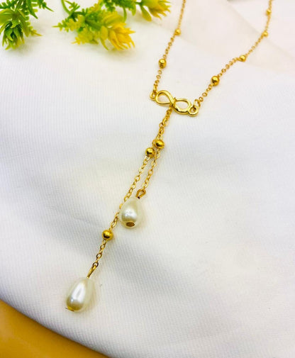 A gold-tone lariat-style necklace with small bead accents, a clasp closure, and two dangling white pearl teardrop charms, displayed on a white textured fabric background with small yellow flowers in the corner.