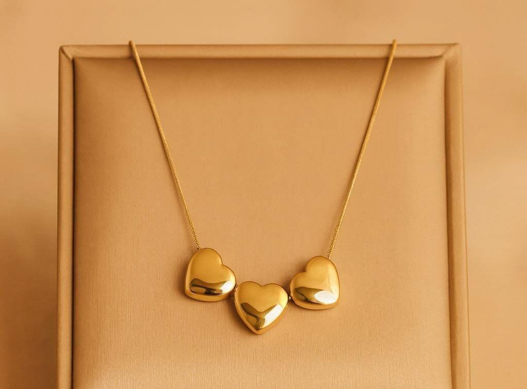 A gold necklace with three small, polished heart-shaped pendants displayed on a textured gold jewelry box.