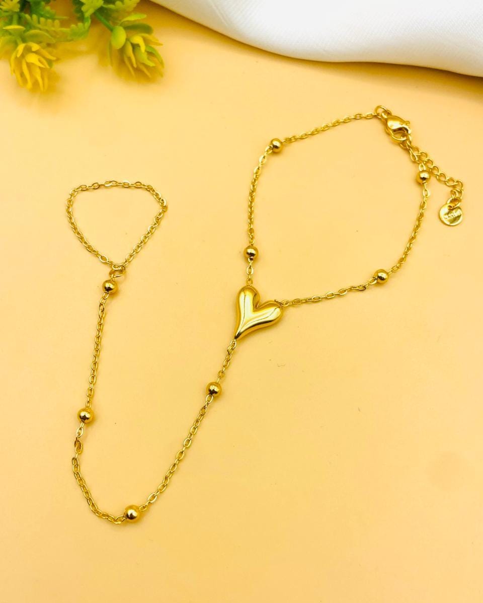 A gold Y-shaped chain necklace with a polished heart-shaped pendant, displayed on a warm peach background with a white fabric corner and small yellow flowers.