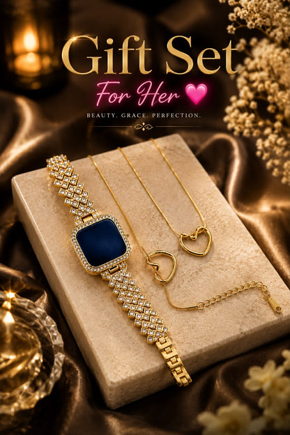 Gold jewelry gift set for her, featuring a watch with a deep blue square face and crystal-encrusted bracelet, a matching gold heart pendant necklace, and a heart-shaped ring, displayed on a beige stone block with decorative gold fabric and flowers.