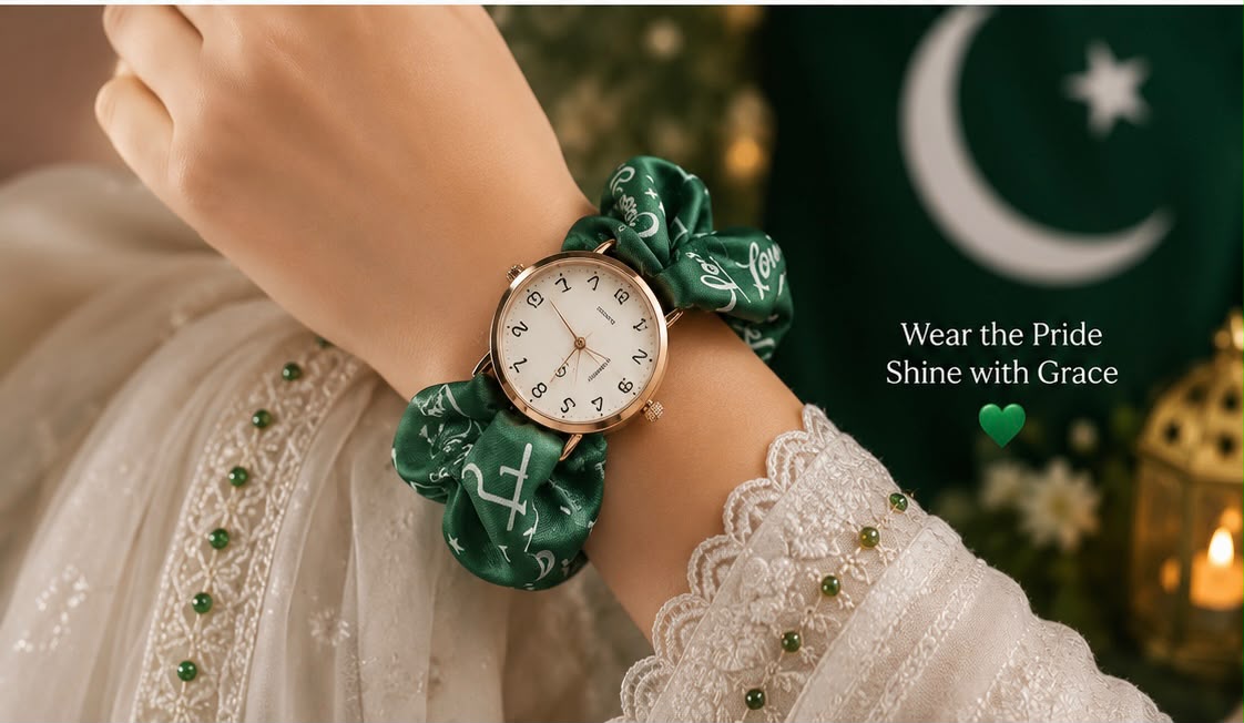 A close-up of a person's wrist wearing a watch with a green satin fabric strap and matching green fabric loops. The watch face is white with black markings and a gold-tone case.