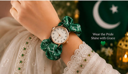 A close-up of a person's wrist wearing a watch with a green satin fabric strap and matching green fabric loops. The watch face is white with black markings and a gold-tone case.