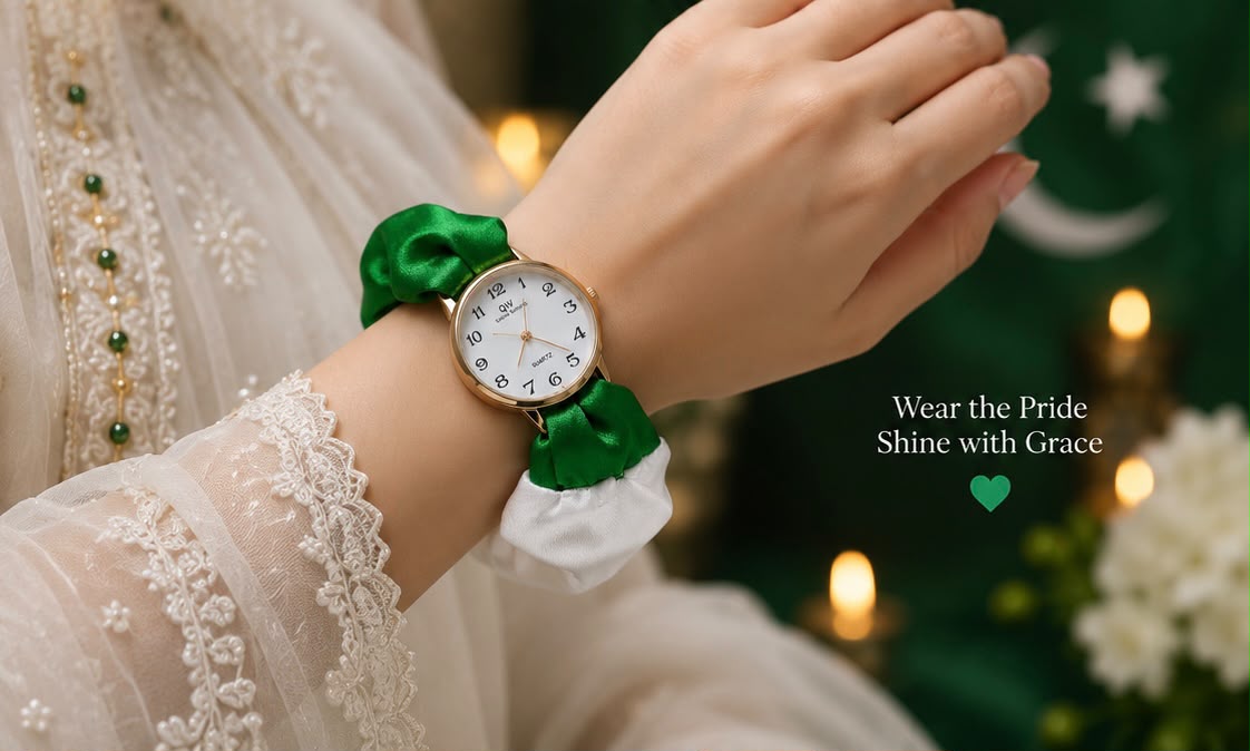A close-up lifestyle shot of a woman's wrist wearing a watch with a white dial and a green satin ribbon bracelet. The person is wearing a white lace-trimmed dress, with a festive green and white background featuring warm bokeh lights and the text 'Wear the Pride Shine with Grace'.
